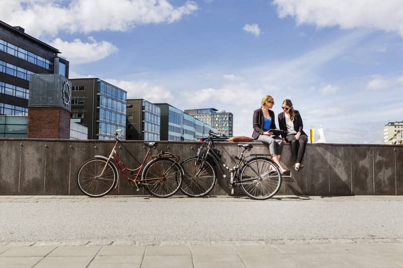 two women with bicycles sitting on wall and talking