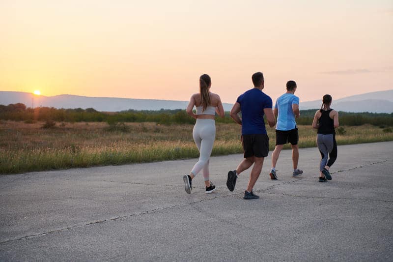 Gruppe junger Läufer joggt im Sonnenuntergang und macht Sport als Ausgleich nach der Arbeit