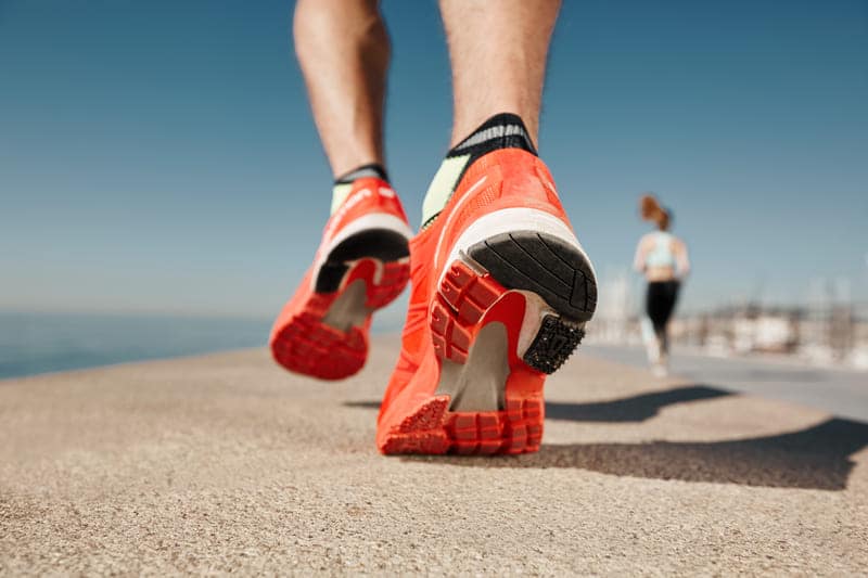 Eine Person läuft in Laufschuhen mit oranger Sohle über den Asphalt