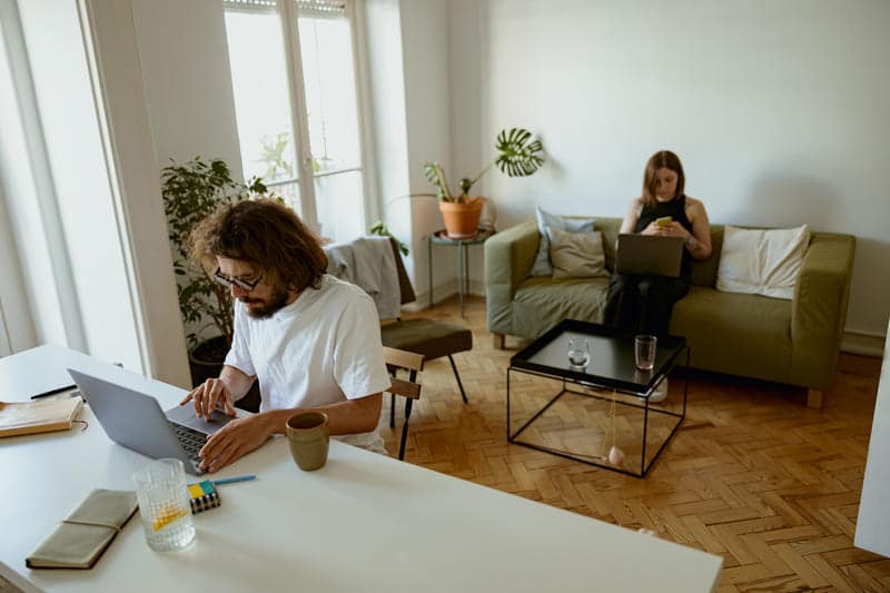 Ein Paar sitzt im Wohnzimmer und arbeitet am Laptop.