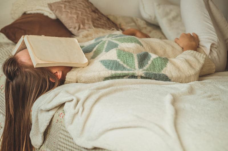 Eine Frau liegt auf dem Bett nach der Arbeit und ein Buch liegt auf ihrem Gesicht