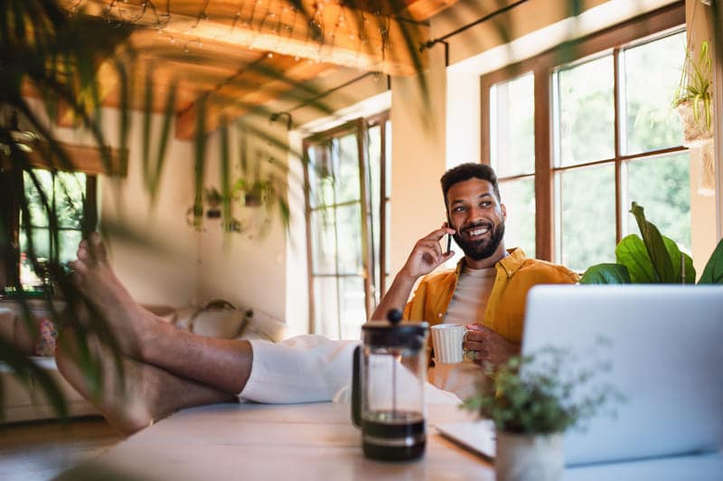 Mann sitzt am Schreibtisch und telefoniert aus dem Home-Office mit den Füßen auf dem Tisch